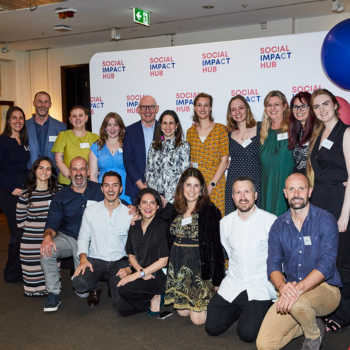 A large group of people posing together in front of a Social Impact Hub branded step-and-repeat banner at an event